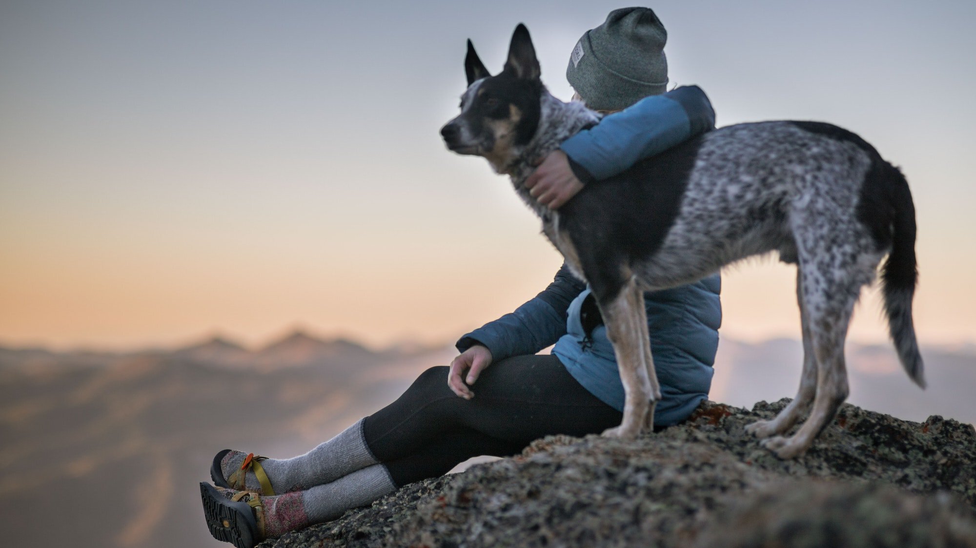 Woman with an arm over her dog enjoying mountain views